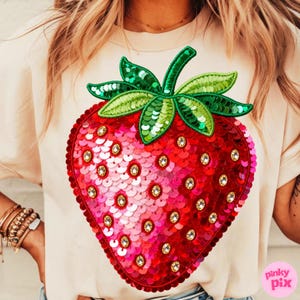 K&ouml;nnte beinhalten: Cremefarbenes T-Shirt mit einem gro&szlig;en Erdbeer-Design aus Pailletten. Die Erdbeere ist rot und rosa mit gr&uuml;nen Bl&auml;ttern und Stiel und mit klaren Strasssteinen verziert. Das Shirt hat kurze &Auml;rmel.