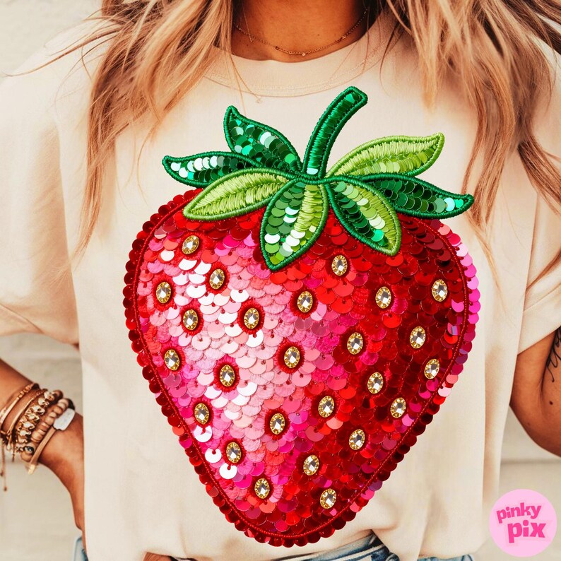 K&ouml;nnte beinhalten: Cremefarbenes T-Shirt mit einem gro&szlig;en Erdbeer-Design aus Pailletten. Die Erdbeere ist rot und rosa mit gr&uuml;nen Bl&auml;ttern und Stiel und mit klaren Strasssteinen verziert. Das Shirt hat kurze &Auml;rmel.