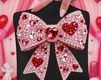 May include: A pink bow-shaped accessory, heavily embellished with rhinestones and heart-shaped gems. The bow is set against a black background, with a large red heart at the center. The accessory is held by a hand with pink nail polish.