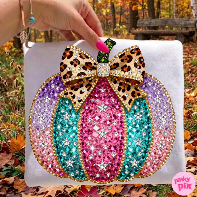 Op de afbeelding: Een pompoenvormige knutseldecoratie bedekt met veelkleurige strass-steentjes, voorzien van een strik met luipaardprint aan de bovenkant. De pompoen toont verticale segmenten van roze, turquoise en paarse kristallen, geaccentueerd met zilveren sterren.
