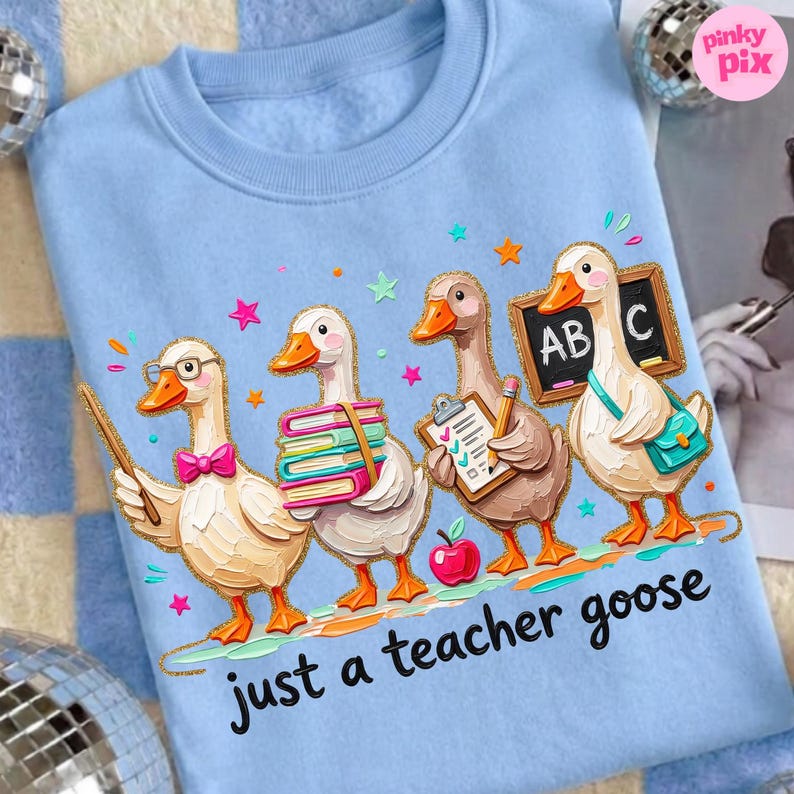 May include: Light blue sweatshirt featuring a whimsical illustration of four geese dressed as teachers. One goose holds a pointer, another carries books, a third has a clipboard, and the last holds a chalkboard. The text "just a teacher goose" is below.