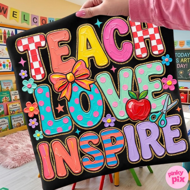 May include: Black decorative pillow with the words "TEACH LOVE INSPIRE" in colorful, textured lettering. The design includes a red apple, scissors, flowers, and a bow. The pillow has a gold glitter border.