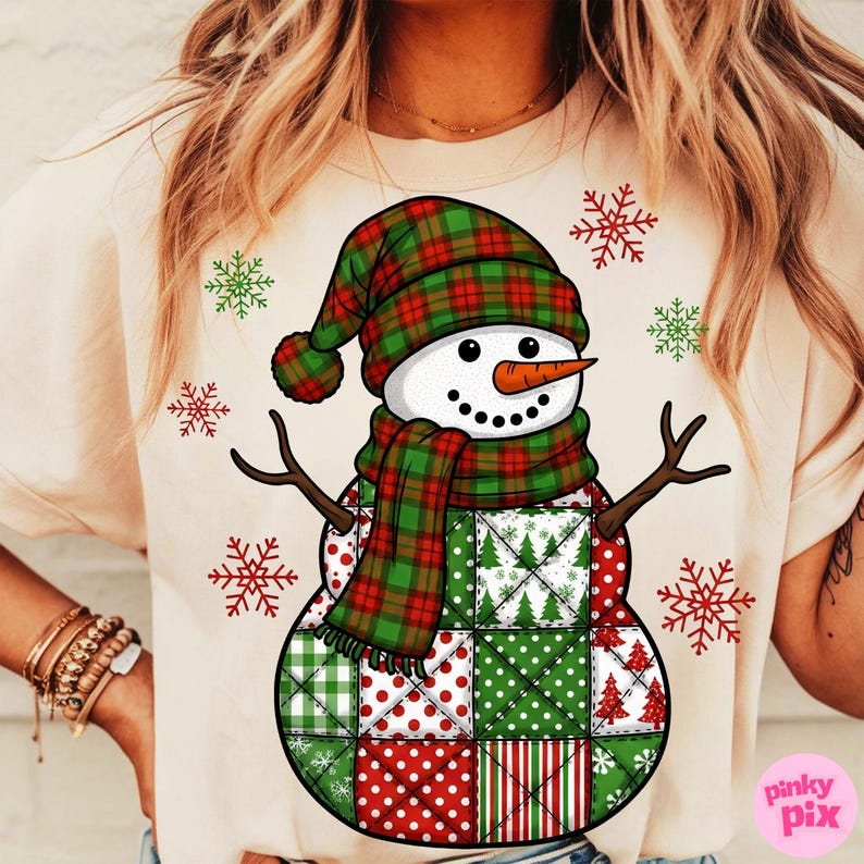 May include: Cream-colored t-shirt featuring a whimsical snowman design. The snowman has a plaid hat and scarf, a carrot nose, and a patchwork body with red and green patterns. Red and green snowflakes surround the snowman.