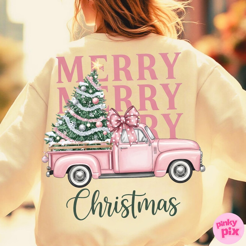 May include: Cream-colored sweatshirt with a pink Christmas truck graphic. The truck bed holds a decorated Christmas tree and is topped with a pink bow. The words "MERRY CHRISTMAS" are printed on the back.