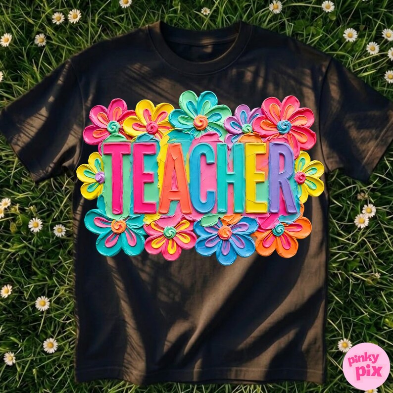 May include: Black t-shirt with a colorful floral design and the word "TEACHER" in vibrant, raised letters. The flowers are in shades of pink, yellow, blue, and orange, creating a cheerful and eye-catching look. The shirt is made of a soft material.