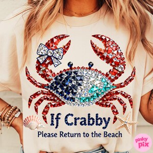May include: A light beige t-shirt featuring a crab design made of red, white, and blue gems. The crab has a bow and the text "If Crabby, Please Return to the Beach". A seashell and starfish are also visible.