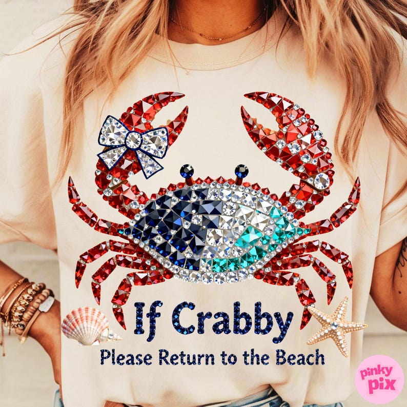 May include: A light beige t-shirt featuring a crab design made of red, white, and blue gems. The crab has a bow and the text "If Crabby, Please Return to the Beach". A seashell and starfish are also visible.