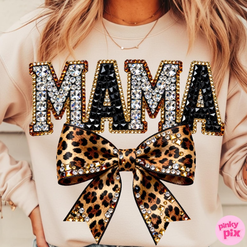 May include: A beige sweatshirt with the word "MAMA" in jeweled letters. The "M" and "A" are outlined in gold and filled with clear rhinestones, while the center "A" is black. A leopard print bow with rhinestone accents is below the text.