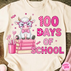 Pu&ograve; includere: T-shirt color crema con una mucca dei cartoni animati con occhiali a forma di stella e un papillon, seduta su libri rosa. La maglietta presenta la scritta "100 Days of School" in rosa, con stelle e grafica di caramelle rosa.