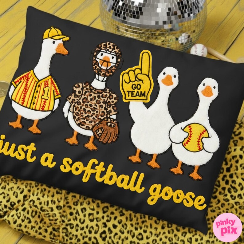 May include: Black pillow with embroidered cartoon geese in baseball uniforms and holding a foam finger. The text "just a softball goose" is embroidered in yellow. A disco ball and baseball are in the background.