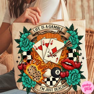 May include: A white canvas tote bag with a colourful graphic design. The design features playing cards, a dart, cherries, a pool ball, dice, and flames. The text on the bag reads "Life is a gamble, I'm just dealing."