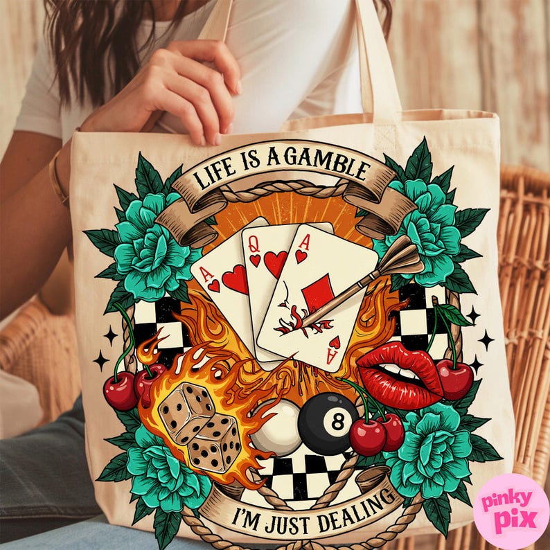 May include: A white canvas tote bag with a colourful graphic design. The design features playing cards, a dart, cherries, a pool ball, dice, and flames. The text on the bag reads "Life is a gamble, I'm just dealing."