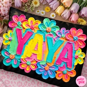 May include: Black pillow with the word "YAYA" in bright, textured paint, surrounded by colorful flowers in shades of pink, yellow, blue, and orange. The pillow is decorated with a floral design, perfect for home decor.