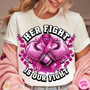May include: White t-shirt with the text "HER FIGHT IS OUR FIGHT" in a black and white font. The design includes pink boxing gloves, a pink ribbon, and pink floral accents. The shirt has a crew neck and short sleeves.