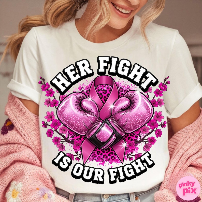May include: White t-shirt with the text "HER FIGHT IS OUR FIGHT" in a black and white font. The design includes pink boxing gloves, a pink ribbon, and pink floral accents. The shirt has a crew neck and short sleeves.