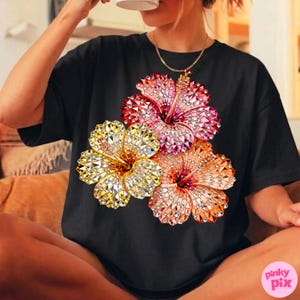 May include: Black t-shirt featuring a vibrant floral design. The graphic showcases three hibiscus flowers in shades of yellow, pink, and orange, each with a sparkling, gem-like texture. The shirt is a casual style.