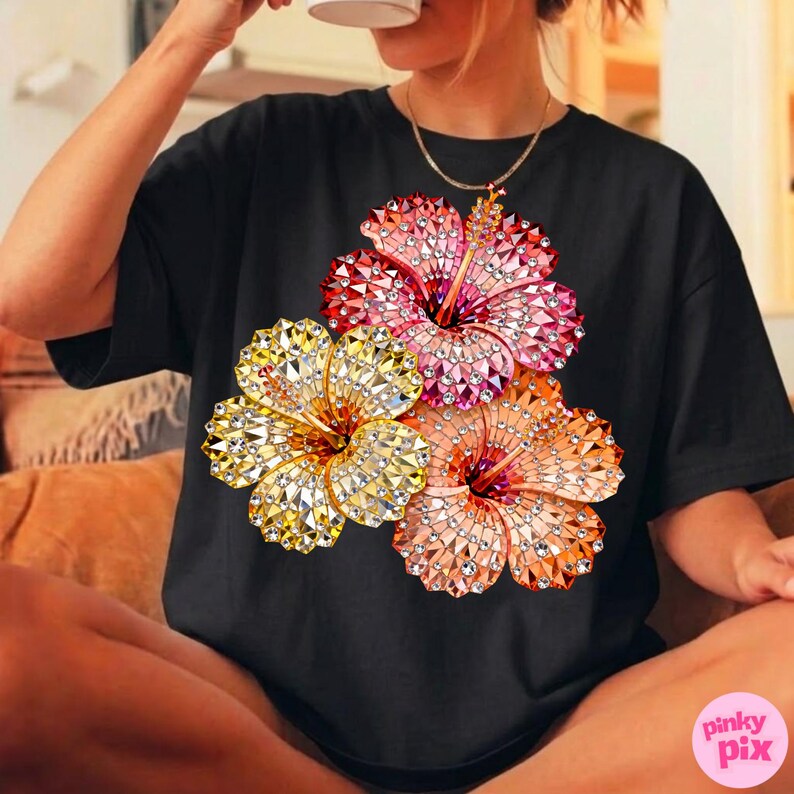 May include: Black t-shirt featuring a vibrant floral design. The graphic showcases three hibiscus flowers in shades of yellow, pink, and orange, each with a sparkling, gem-like texture. The shirt is a casual style.