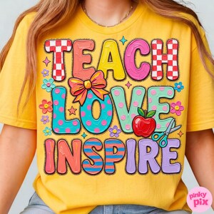 May include: Yellow t-shirt with the words "TEACH LOVE INSPIRE" in colorful, playful lettering. The design includes a red apple, scissors, flowers, and a bow. The shirt is a casual, short-sleeved style.