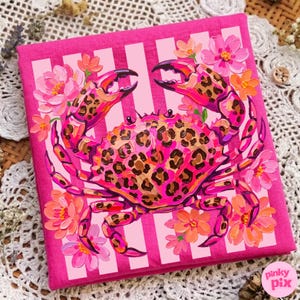 May include: A pink square canvas featuring a crab with a leopard print pattern on its shell and claws. The crab is surrounded by pink and orange flowers. The background has vertical white stripes.