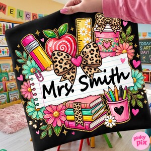 May include: Black teacher-themed design featuring a pencil, apple, ruler, coffee cup, books, and pencils. The design includes a leopard print bow and the name "Mrs. Smith" on a lined paper background. Floral accents and hearts complete the design.