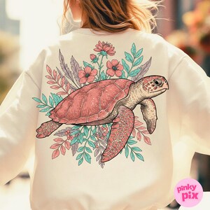 May include: A cream-colored sweatshirt with a pink and green floral design featuring a sea turtle. The turtle is outlined in black and has a detailed shell.