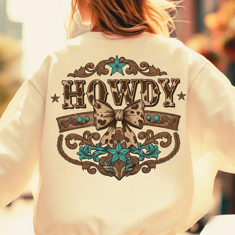 Pu&ograve; includere: Una felpa color crema con un designo marrone e turchese che presenta la parola "HOWDY" con un fiocco e stelle.