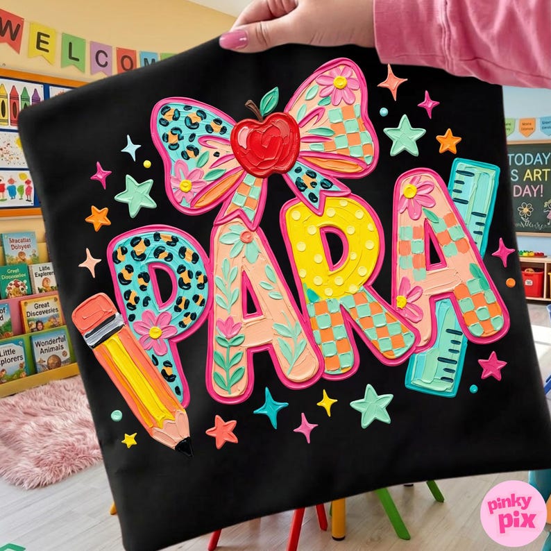 May include: Black tote bag with the word "PARA" in colorful, layered letters. The design includes a bow with an apple, a pencil, stars, and ruler accents. The letters have floral, leopard, and checkered patterns.