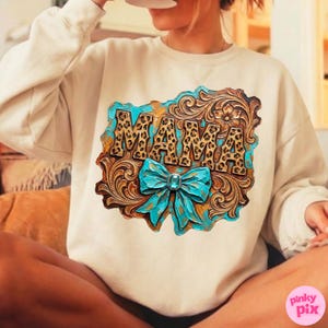 May include: Cream-colored sweatshirt featuring a decorative design with the word "MAMA" in a leopard print font. The design includes a turquoise bow and floral accents, set against a brown, textured background.