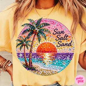 May include: Yellow t-shirt with a vibrant, circular graphic. The graphic features a sunset scene with palm trees, ocean waves, and the words "Sun Salt Sand" in a decorative font. The design is embellished with sparkling rhinestones.