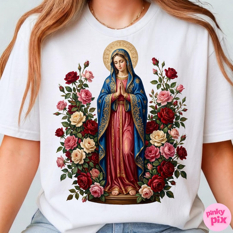 May include: White t-shirt featuring a religious illustration of a woman in a blue and pink robe, surrounded by roses in shades of red, pink, and cream. The woman has a gold halo and is in a prayerful pose.