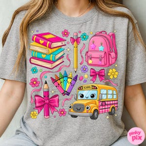 Pu&ograve; includere: Una maglietta grigia con una grafica colorata a tema scolastico. Il design include uno zaino rosa, libri, matite, pastelli, fiori e un autobus scolastico giallo con la scritta "SCHOOL".