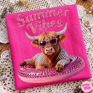 May include: A hot pink t-shirt featuring a rhinestone-studded Highland cow wearing sunglasses and a bejeweled floatie. The text "Summer Vibes" is written across the top in rhinestones. The image has a fun, summer theme.