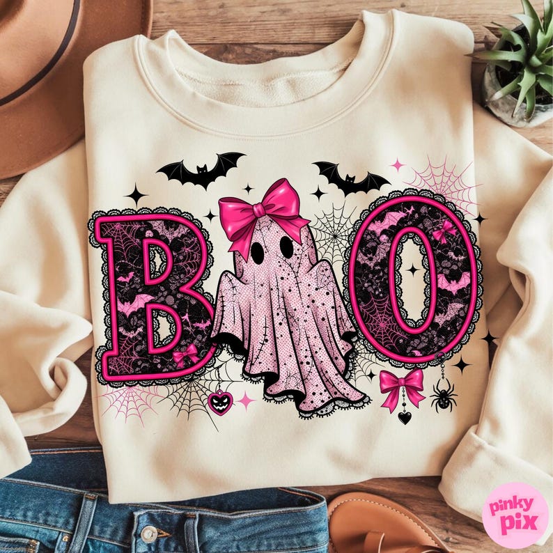 Puede incluir: Sudadera de color crema con un dise&ntilde;o tem&aacute;tico de Halloween. La palabra "BOO" est&aacute; escrita en rosa, con letras ribeteadas de encaje. Un fantasma rosa con un lazo est&aacute; en el centro. Murci&eacute;lagos, telara&ntilde;as y otros elementos de Halloween completan el dise&ntilde;o.