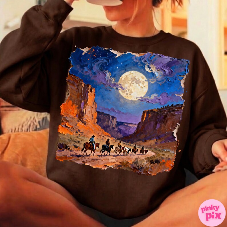 May include: Brown sweatshirt featuring a vibrant, artistic depiction of a desert landscape under a full moon. The artwork shows cowboys on horseback, riding through a canyon. The color palette includes blues, oranges, and browns.