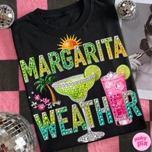 Peut inclure: T-shirt noir avec l'inscription "Margarita Weather" en strass verts, jaunes et bleus. Le motif comprend un verre &agrave; margarita, un cocktail rose, un palmier et un soleil.
