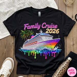Op de afbeelding: Zwart t-shirt met een kleurrijke afbeelding van een cruiseschip, palmbomen en de tekst "Family Cruise 2026". Het schip heeft een regenboogontwerp en sprankelende details, met druipende watereffecten.
