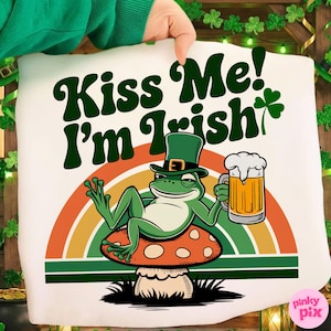 Puede incluir: Funda de almohada blanca con un diseño del Día de San Patricio. El diseño presenta una rana verde con sombrero de copa, sosteniendo una cerveza y descansando sobre una seta. El texto dice "Kiss Me! I'm Irish" en verde.