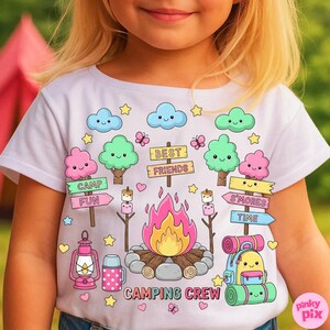 May include: White t-shirt with a colorful camping-themed graphic. The design includes a campfire, trees, clouds, stars, and the words "CAMPING CREW", "BEST FRIENDS", "CAMP FUN", and "S'MORES TIME". The shirt has a crew neck and short sleeves.