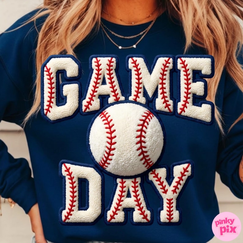 May include: Navy blue sweatshirt with the words "GAME DAY" in white, baseball-themed lettering. A baseball is centered on the sweatshirt. The lettering and baseball have red stitching details. The sweatshirt is a casual style.