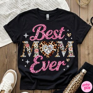 May include: Black t-shirt with the text "Best MOM Ever" in pink and patterned letters. The heart in the word "MOM" has a leopard print design with a diamond in the center. Floral and diamond accents complete the design.