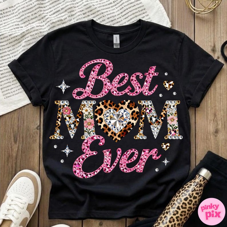 May include: Black t-shirt with the text "Best MOM Ever" in pink and patterned letters. The heart in the word "MOM" has a leopard print design with a diamond in the center. Floral and diamond accents complete the design.