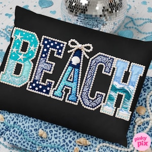 May include: Black rectangular pillow with the word "BEACH" embroidered in a variety of blue patterns and textures. The letters are outlined with white pearls. The letter "A" features a seashell and bow.