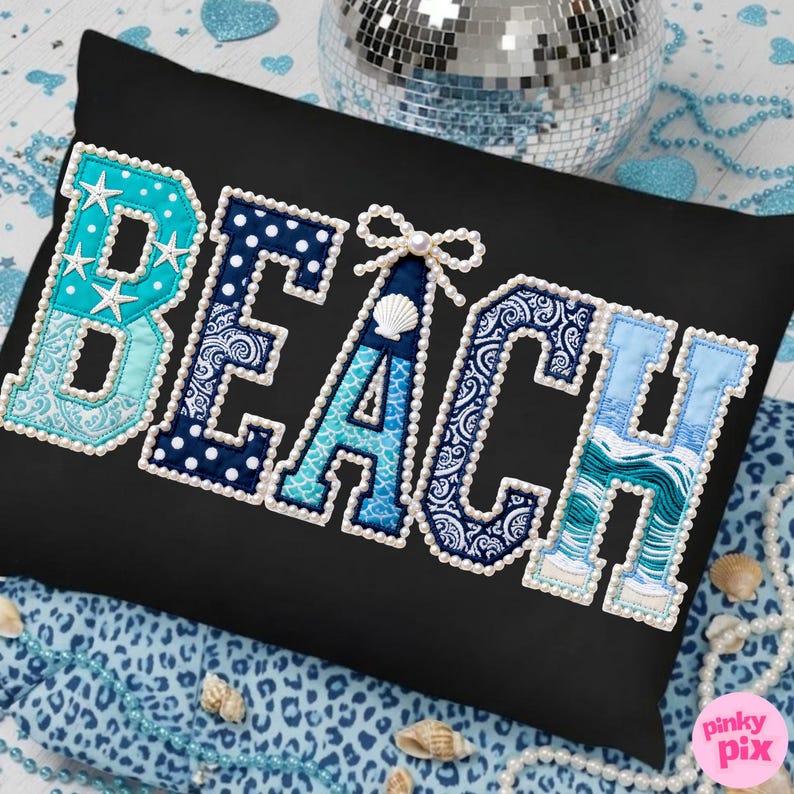 May include: Black rectangular pillow with the word "BEACH" embroidered in a variety of blue patterns and textures. The letters are outlined with white pearls. The letter "A" features a seashell and bow.