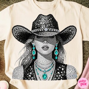May include: Cream-colored t-shirt featuring a detailed graphic of a woman wearing a bedazzled cowboy hat and jewelry. The design is primarily black, white, and silver, with accents of turquoise. The image has a mosaic-like appearance, creating a glamorous aesthetic.