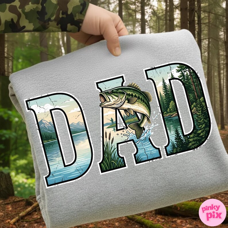 Pu&ograve; includere: Una coperta in pile grigia con la scritta "DAD" a grandi lettere. La "A" presenta un pesce persico che salta e schizzi d'acqua. Le lettere sono riempite con un paesaggio di lago e alberi.