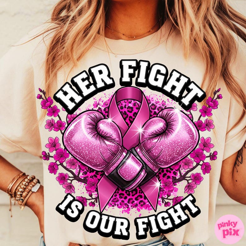 May include: A beige t-shirt featuring a design with the text "HER FIGHT IS OUR FIGHT". The design includes pink boxing gloves, a pink ribbon, and pink floral accents. The design has a leopard print background.