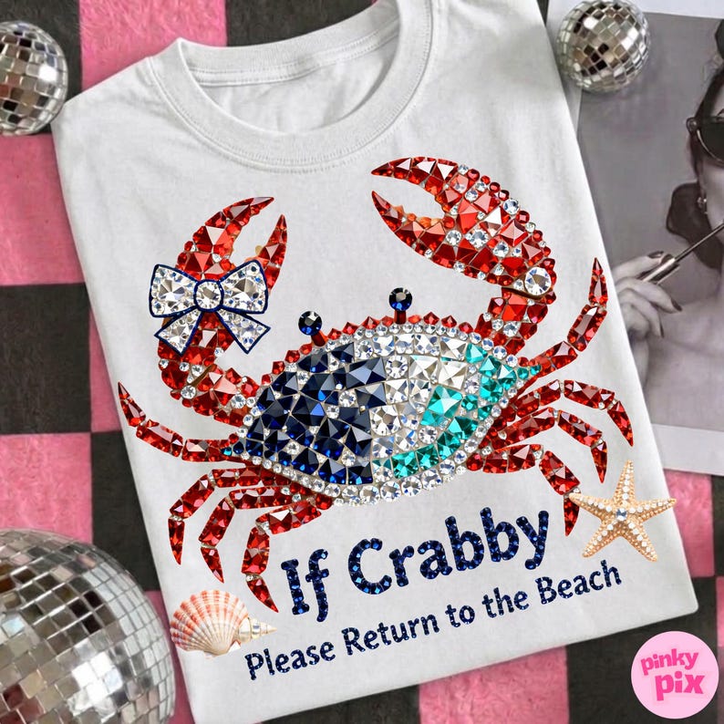 May include: White t-shirt featuring a crab design made of red, blue, and clear rhinestones. The crab has a blue and white bow. Text on the shirt reads "If Crabby Please Return to the Beach."