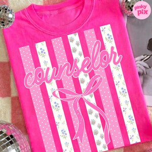 May include: A bright pink t-shirt with the word "counselor" in a cursive font. The shirt features vertical stripes in varying shades of pink, some with polka dots and floral patterns. A pink bow is at the bottom.