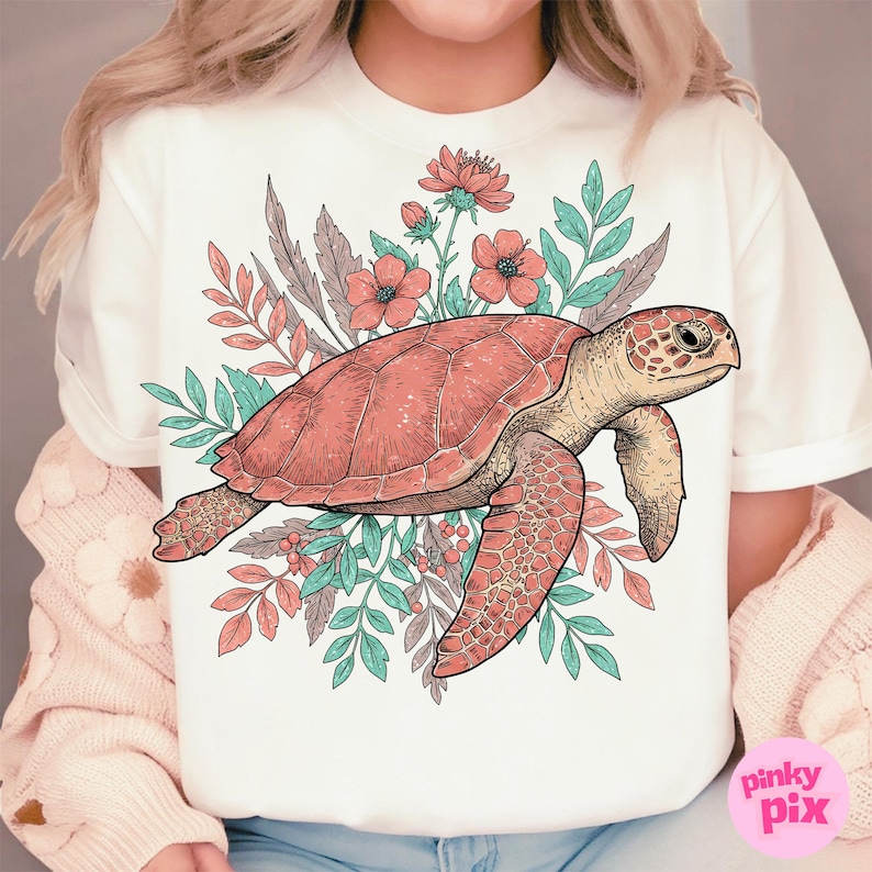 May include: A white t-shirt with a pink and green floral design featuring a sea turtle. The turtle is outlined in black and has a pink shell. The flowers are pink and white with green leaves.
