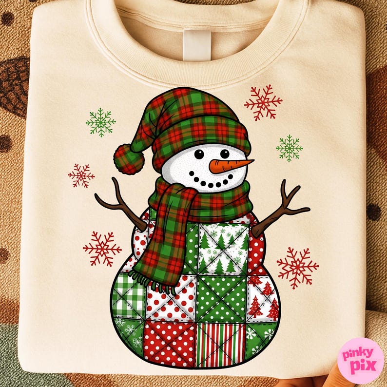 May include: Cream-colored sweatshirt featuring a snowman design. The snowman has a plaid hat and scarf in red and green. The snowman's body is made of patchwork squares in red and green. Snowflakes are scattered around the snowman.